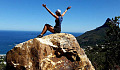 hiker sitting on top of a huge rock with arms up in the air in triumph